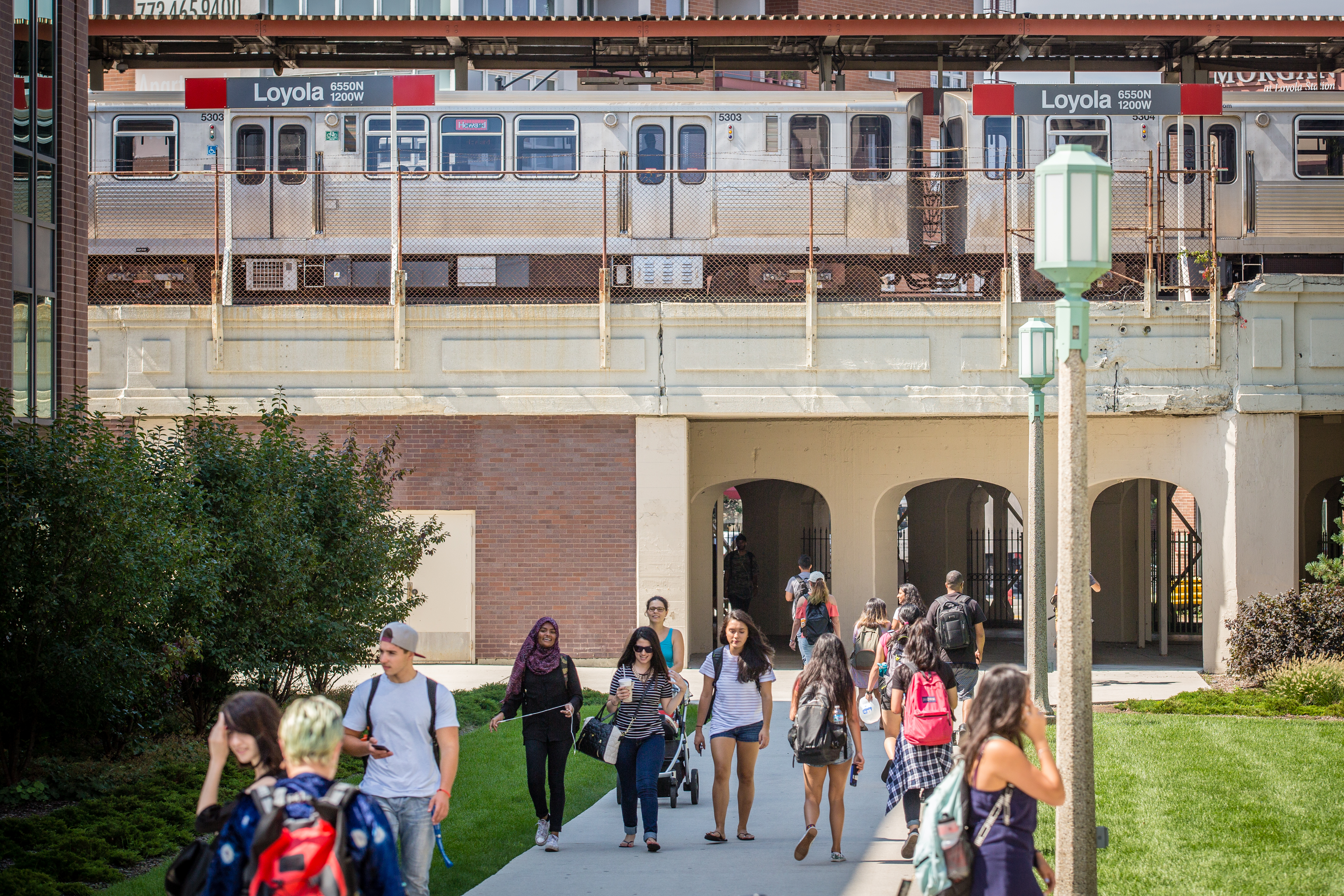 Photo shows students walking by Damen Hall with Red Line platform in the background.